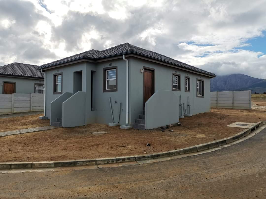 Grey house with wooden door and steps leading to the entrance in affordable housing in Paarl